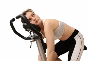 Isolated tired young woman siting on spinning bicycle